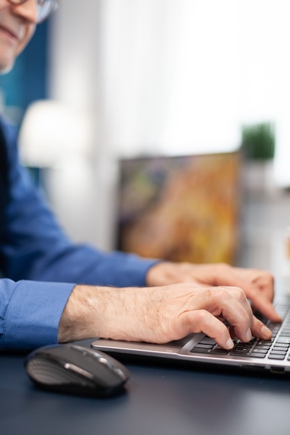 Close up of senior man hands typing on laptop keyboard