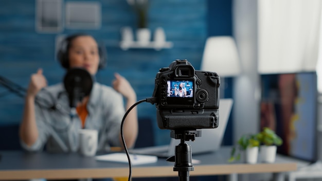 Close up shoot of professional camera recording vlogger talking to audience. Famous social media influencer filming vlog for internet video sharing platforms while sitting at home studio desk.