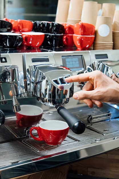 Close-up shot of barista holding filter holder while coffee machine brewing fresh espresso into glass