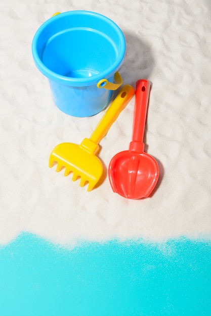 Close-up shot of blue bucket with shovel and rake on sand