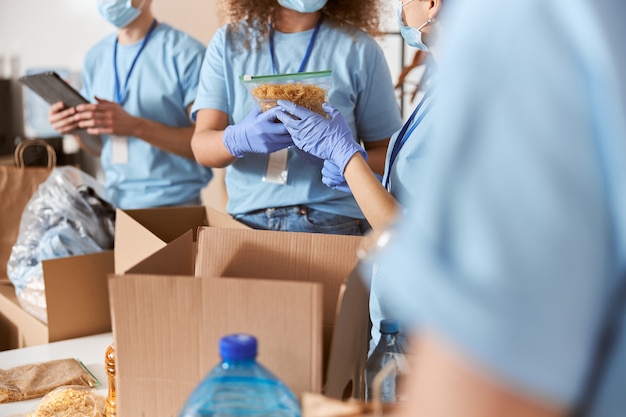 Close up shot of busy volunteers wearing blue uniform protective masks and gloves sorting donated