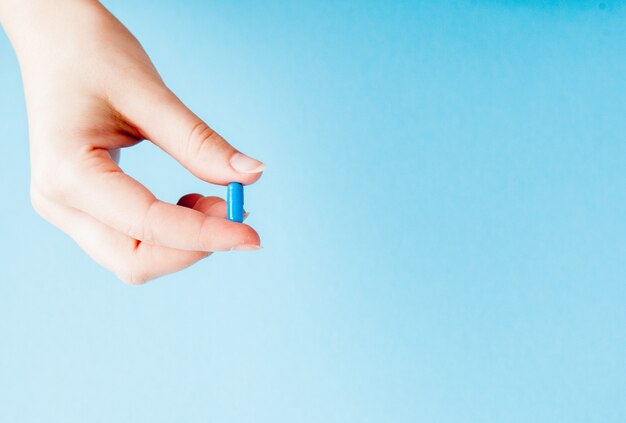 Close-up shot of capsule in nurse's hand isolated over blue wall