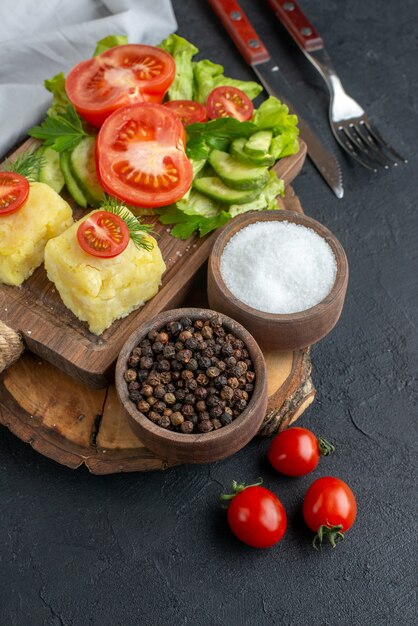 Close up shot of chopped and whole fresh vegetables cheese on cutting board and spices cutlery set on black surface