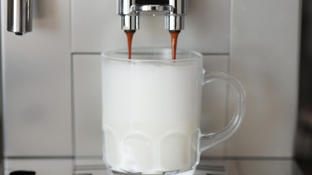 Close up shot of coffee pouring into glass cup with milk making cappuccino using the automatic coffee machine Beverage drink for breakfast