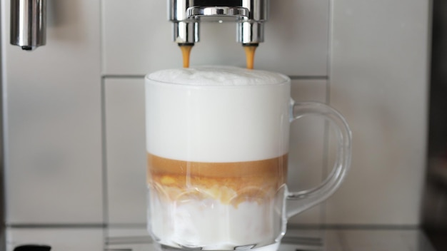 Close up shot of coffee pouring into glass cup with milk making cappuccino using the automatic coffee machine Beverage drink for breakfast