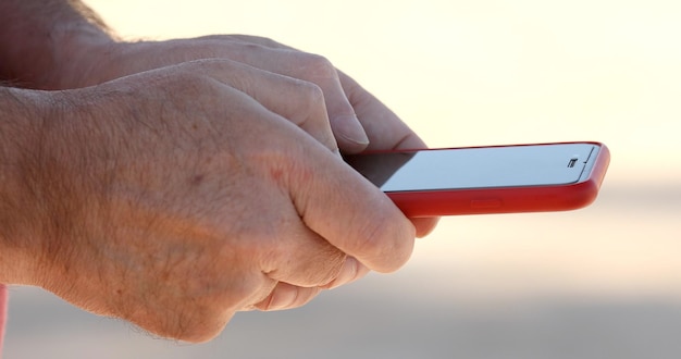 Close-up shot of elderly man's hand using a smartphone outdoor.