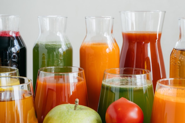 Close up shot of glass bottles filled with colorful juice made of various vegetables and fruit red tomato and green apple in foreground Fresh detox drink