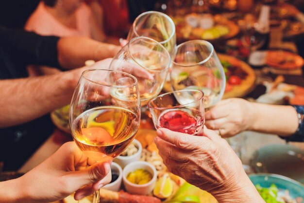 Close up shot of group of people clinking glasses with wine or champagne in front of bokeh background older people hands