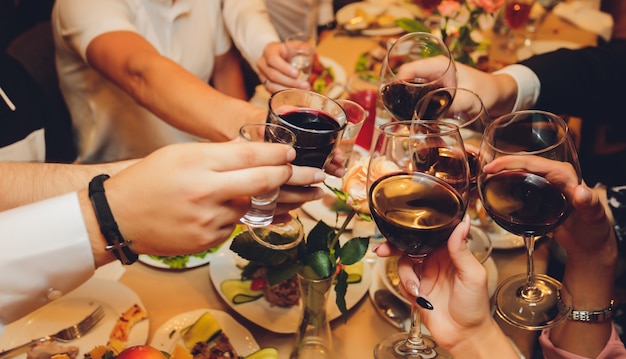 Close up shot of group of people clinking glasses with wine or champagne in front of bokeh background. older people hands.