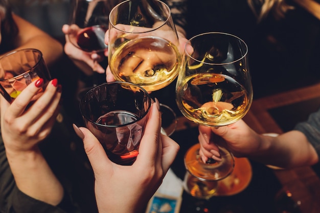 Close up shot of group of people clinking glasses with wine or champagne