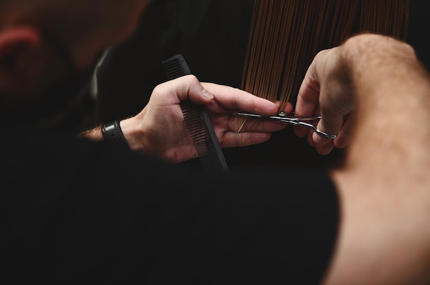 Close-up shot of hairdresser combing and cutting hair of client in beauty parlor. Beauty industry