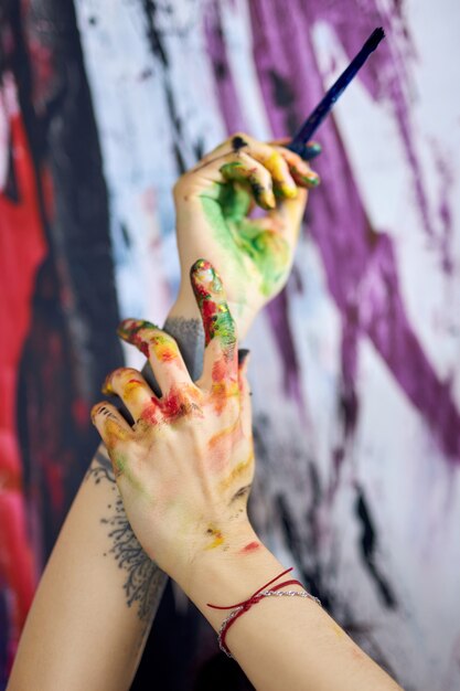 Close up shot of hands in colorful paints of female painter creating abstract painting in workshop