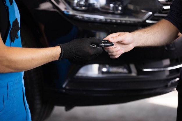 Close up shot of hands of mechanic giving car key to male client after servicing in auto repair shop