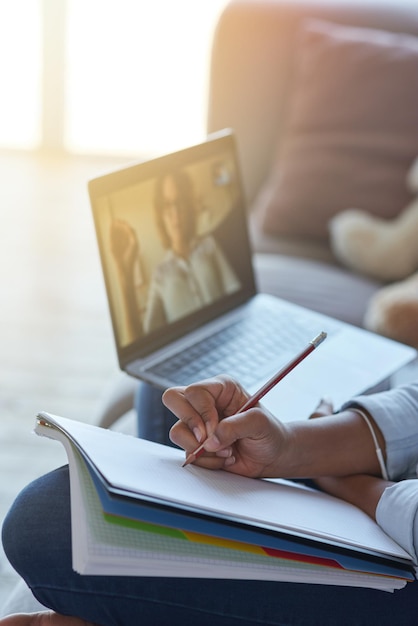 Close up shot of hands of teen schoolgirl making notes while having online lesson with teacher via