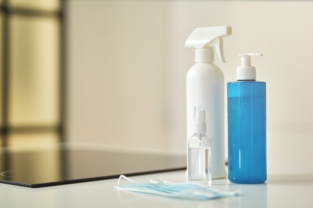 Close up shot of protective face mask and sanitizer bottles to clean surfaces in the kitchen