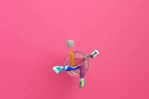 Close up shot of set of multicolored toothbrushes in a glass on pink background