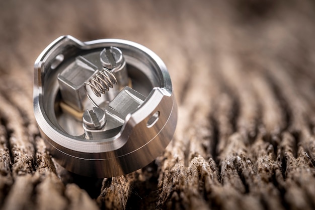 Close up shot of single space coil in high end rebuildable dripping atomizer for flavour chaser on rustic natural wood texture background, vaping device