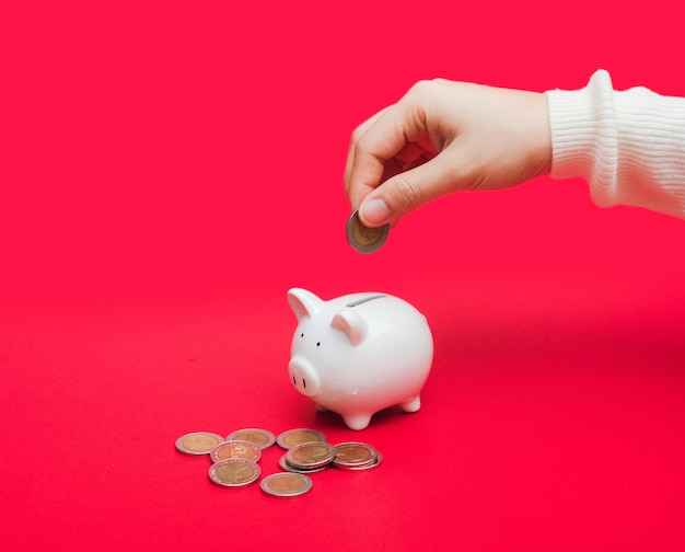 Close up shot of woman hand putting money coin into piggy