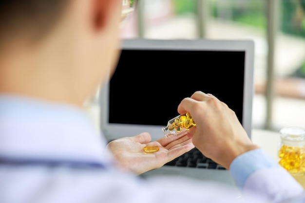 Close up and silective focus rear viev doctor hands holding Omega3 pills and laptop computor