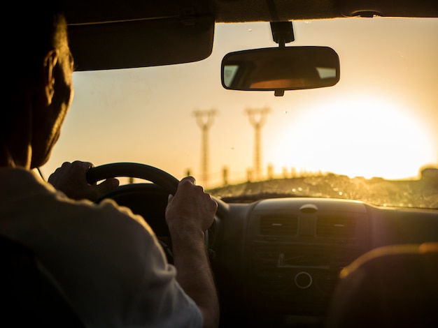 Close up silhouette of man driving a car on a sunset during golden hour