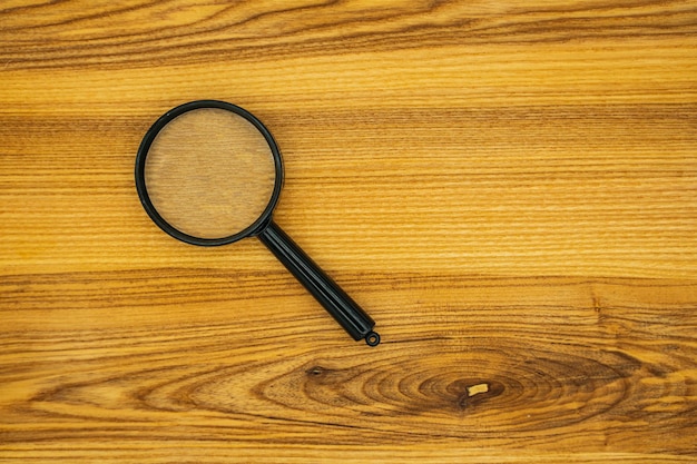 Close up Single Magnifying Glass with Black Handle on the Wooden Table