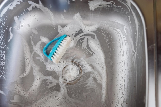 Close up sink drain and kitchen brush. Cleaning metallic sink housework concept