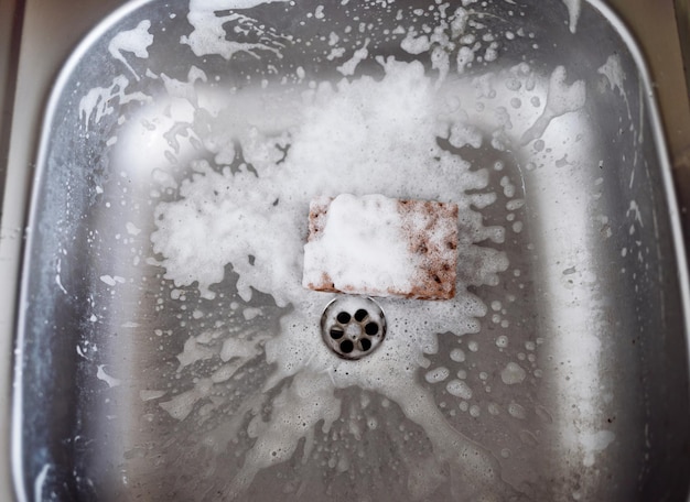 Close up sink drain and sponge. Cleaning metallic sink housework concept