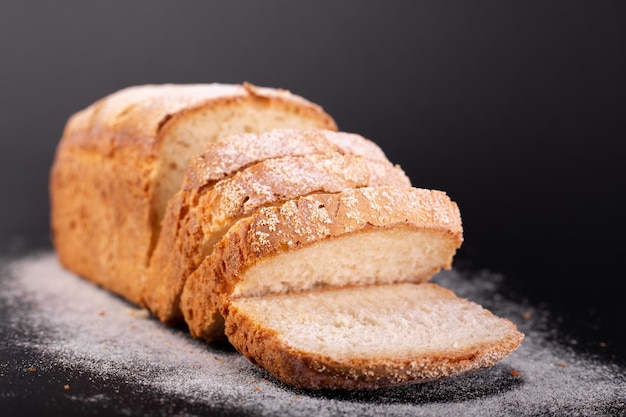 Close up sliced french lean bread with flour on a black background Concept recipe of handmade bread