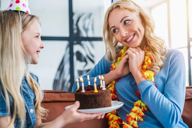 Close up of small girl kid presenting birthday cake to her mom at home