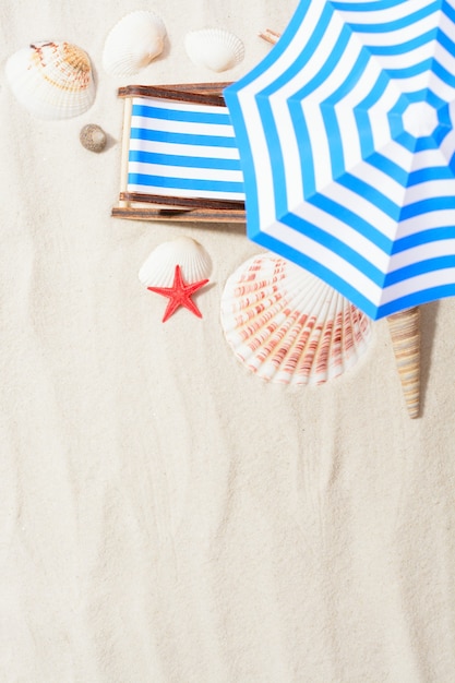 Close-up of small lounge sun bed and sea shells in arrangement on sand