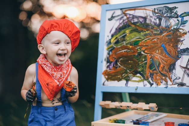 Close up of smile painter boy. The hands of the artist's boy, who paints an oil painting on the nature in sunset