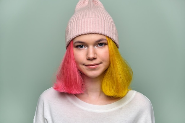 Photo close-up smiling female positive face, portrait of trendy teenager girl with colored dyed hair, young hipster in knitted hat on green pastel background. adolescence, fashion, hair, beauty, lifestyle