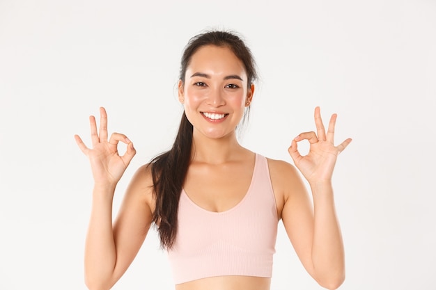 Close-up of smiling, satisfied asian sportswoman recommend gym or yoga classes, showing okay gesture, pleased.