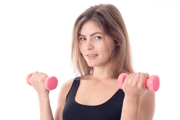 Close-up of a smiling sporty girl who holds in her hands the two little pink dumbbells and looking straight