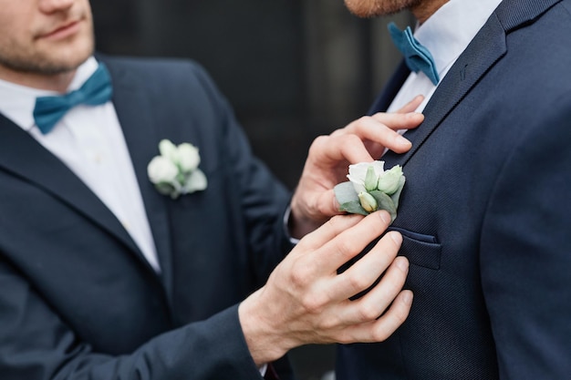 Close up of smiling young man fixing grooms boutonniere during wedding ceremony same sex marriage co