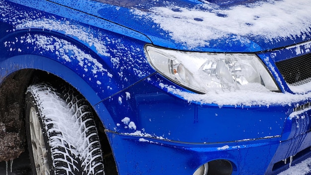 Close-up of snow covered blue suv car under blizzard. Cold winter frosty snowy background.