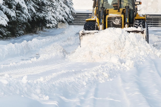 Close up of snowplow plowing road during storm winter snow removal yellow large tractor removing