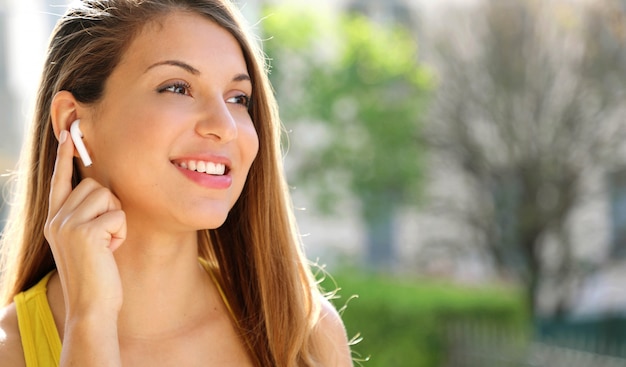 Close up of a sporty smiling girl connecting wireless earphones outside. Looking to the side copy space area.