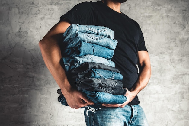 Close up stack of folded denim blue jeans in hand over gray wall background, copy space