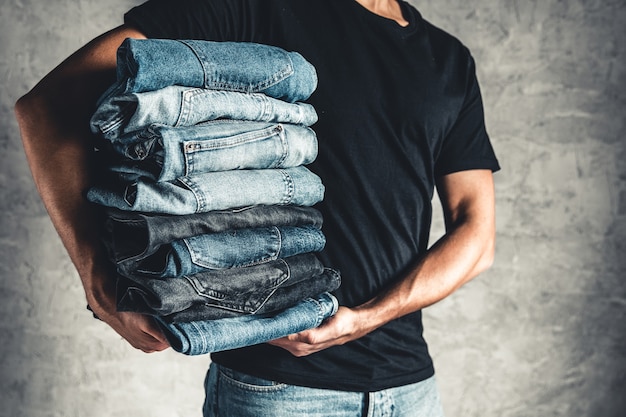 Close up stack of folded denim blue jeans in hand over gray wall background, copy space