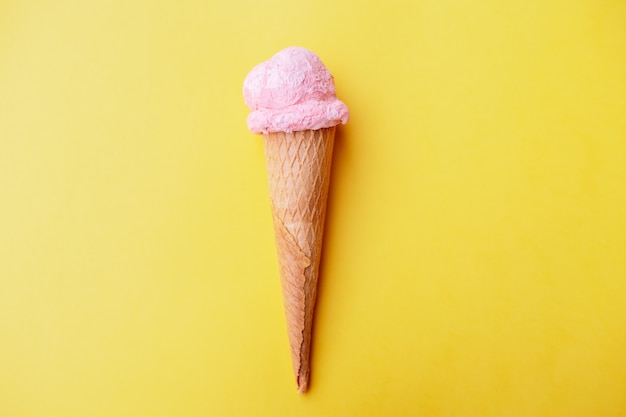 Close up strawberry ice cream in waffles cone against yellow background. Copy space.