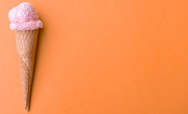 Close up strawberry ice cream in waffles cone on orange background. Copy space.