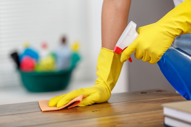 Close up studio shot of housekeeper. Beautiful woman cleaning table with spray. Woman wearing gloves. Focus on hands