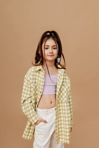 Close-up of a stylish little girl in summer clothes on a beige wall