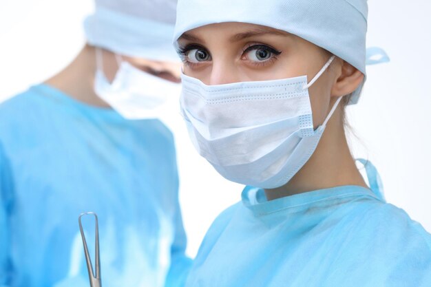 Close up of surgeon woman looking at camera while colleagues performing in background in operation room isolated