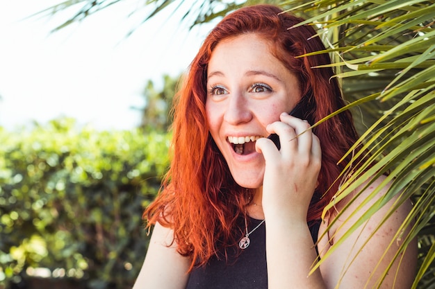 Close up of surprise girl with redhead talking on mobile phone while standing outdoors