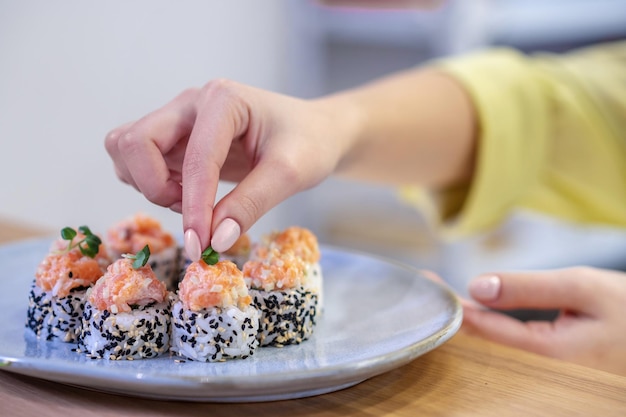 Close up of sushi on the plate and womans hands putting topping