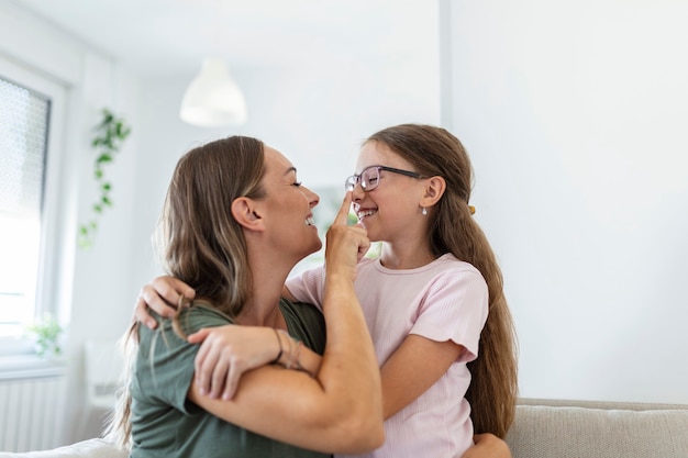 Close up of sweet pretty daughter cuddling with her young mother. Lovely mother embracing her cute daughter on the sofa at home.