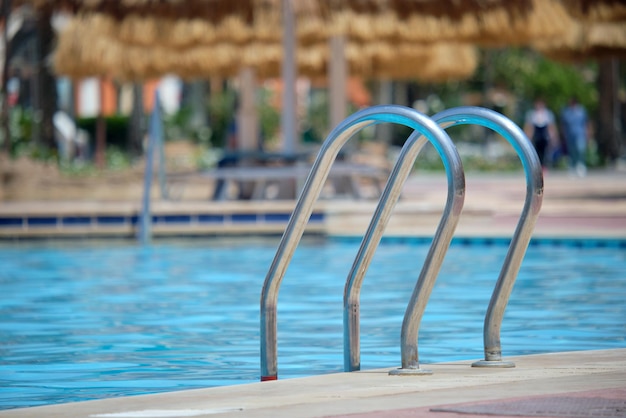 Close up of swimming pool stainless steel handrail descending into tortoise clear pool water. Accessibility of recreational activities concept.