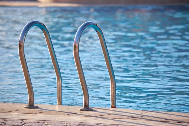 Close up of swimming pool stainless steel handrail descending into tortoise clear pool water Accessibility of recreational activities concept